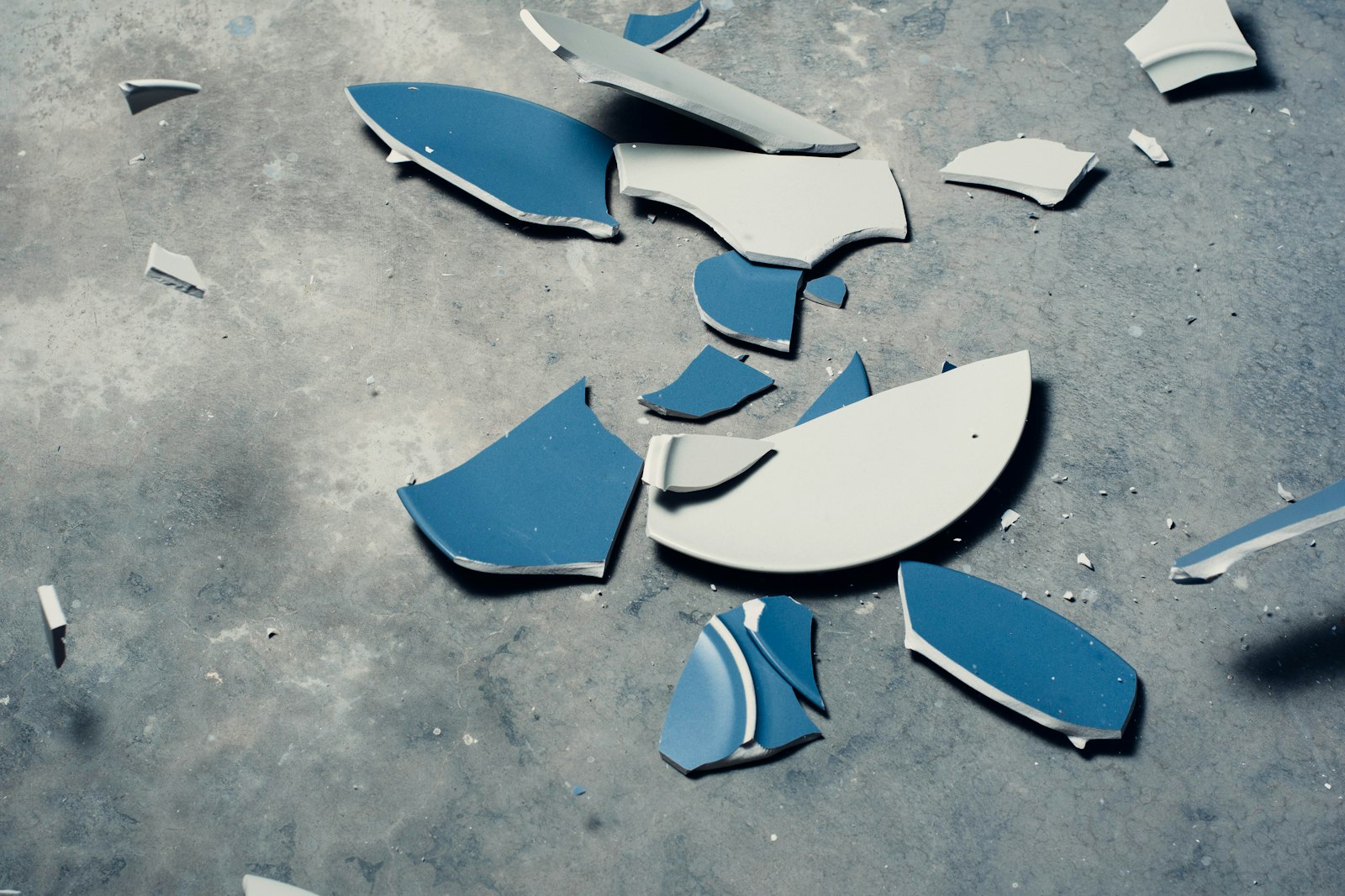 Rage Room NRW – zerbrochene blau-weiße Teller auf grauem Betonboden