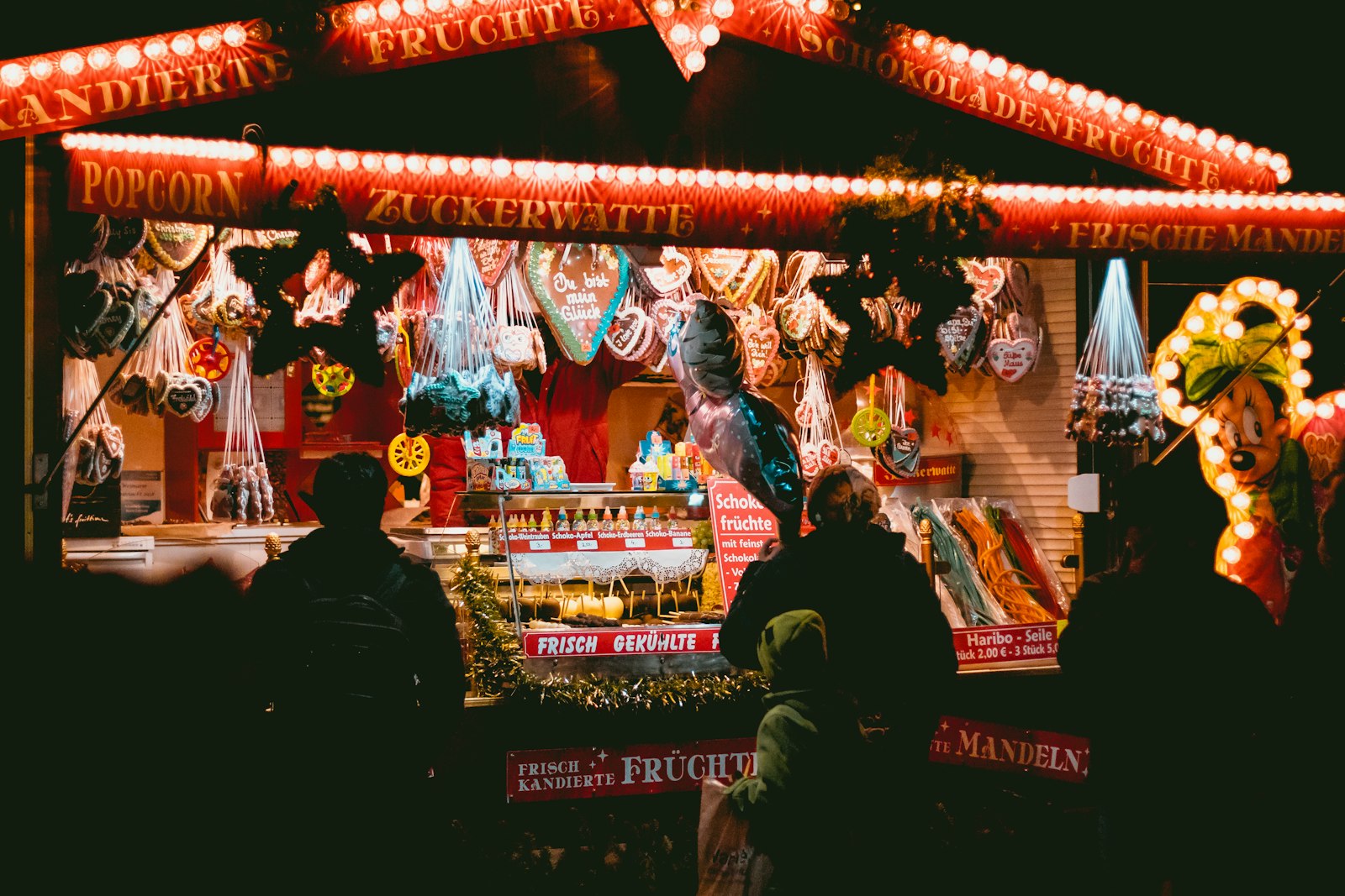 weihnachtsmarkt münster – beleuchteter Süßwarenstand mit Lebkuchenherzen am Abend (Symbolbild)
