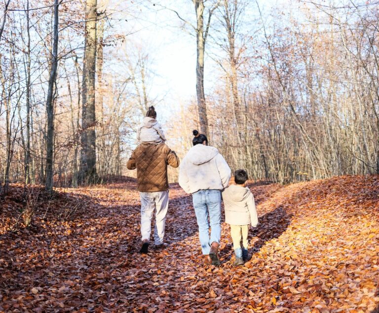 Eifel mit Kindern – Familie wandert von hinten gesehen auf einem laubbedeckten Waldweg im Herbst