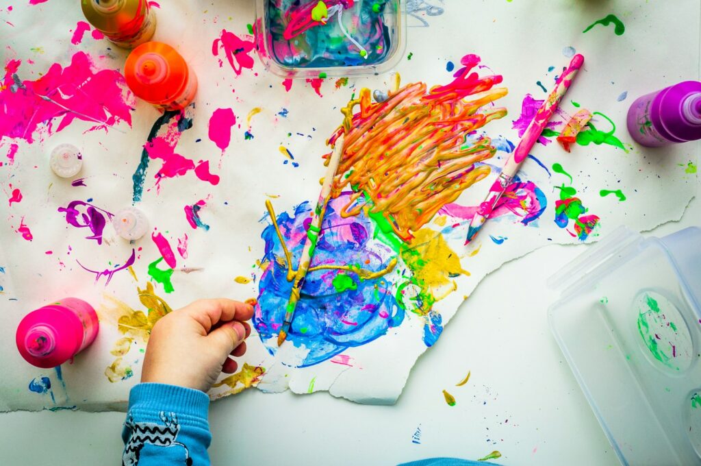 Kinderhand malt mit bunten Farben auf Papier, wie bei einem Geburtstags-Workshop im Museum