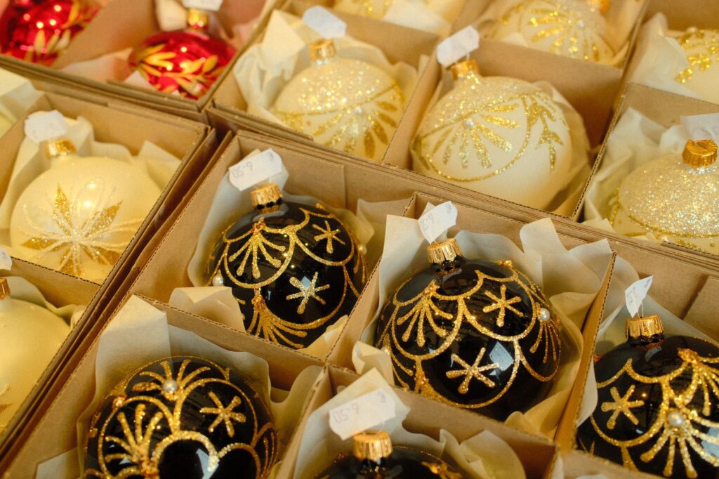 Symbolbild: Christbaumkugeln aus Glas in Schwarz, Creme und Rot mit goldenem Dekor, einzeln in Kartonfächern