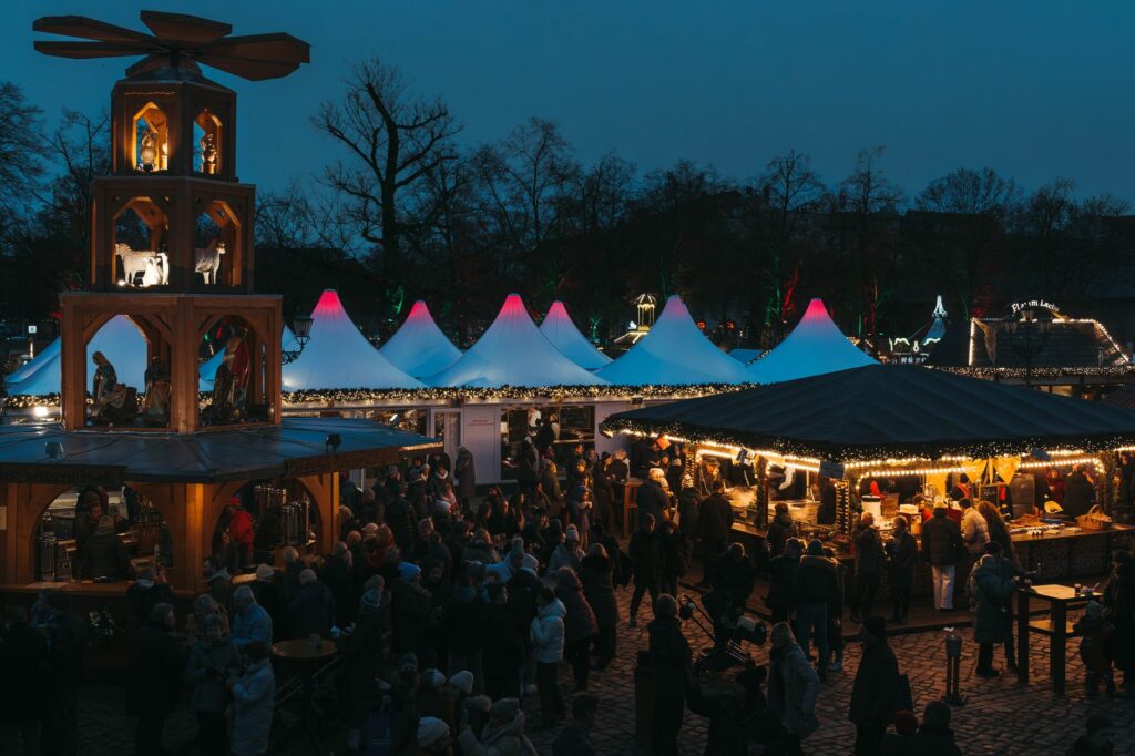 Abendstimmung auf einem Weihnachtsmarkt mit beleuchteten Hütten und Weihnachtspyramide